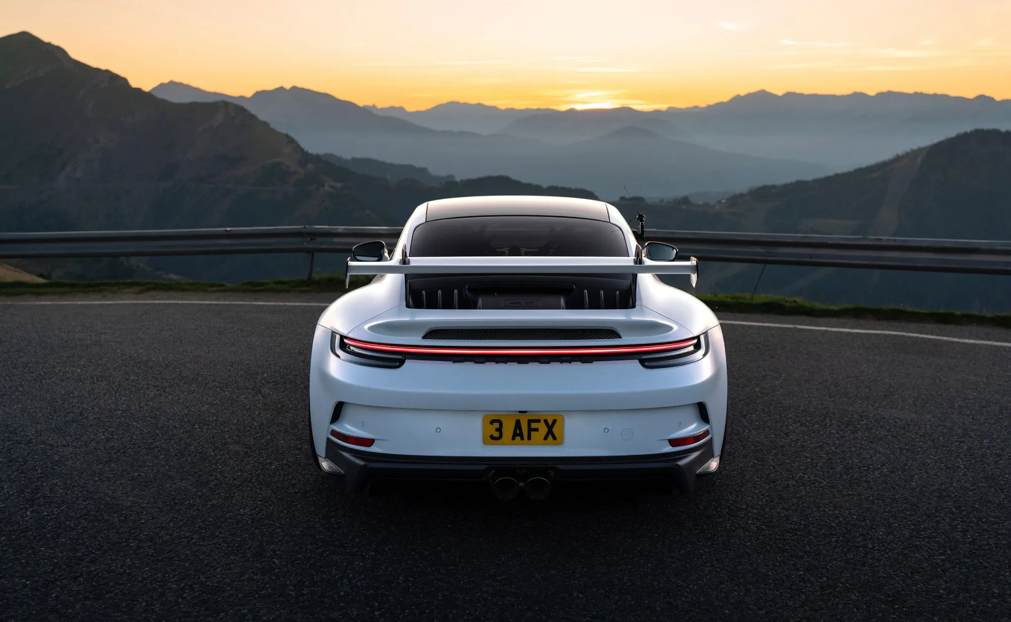 A white Porsche 911 GT3 parked at a mountain pass at dusk, facing the ranges beyond.